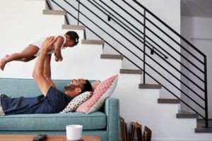 father lying on sofa at home lifting baby daughter