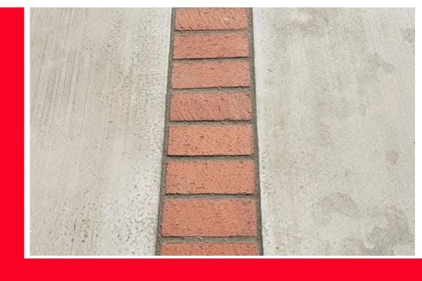 A close-up view of a strip of red bricks set into a wider expanse of grey, lightly textured concrete, creating a decorative border or pathway. A close-up view of a strip of red bricks set into a wider expanse of grey, lightly textured concrete, creating a decorative border or pathway.