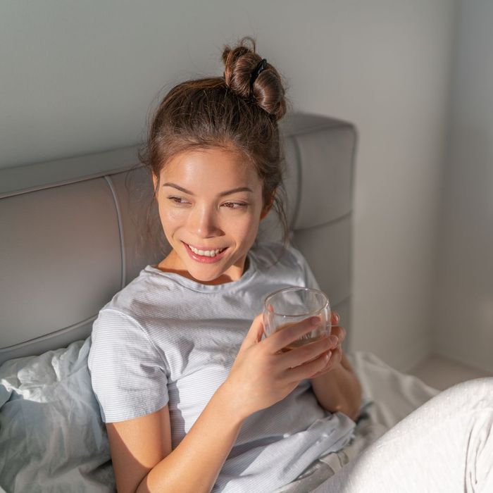 person smiling in bed holding a tea cup
