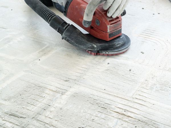 A construction worker uses a power concrete grinder for removing tile glue and resin during renovation work. 