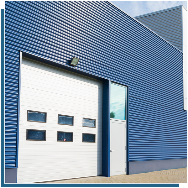 closed white commercial garage door with windows on blue-sided building