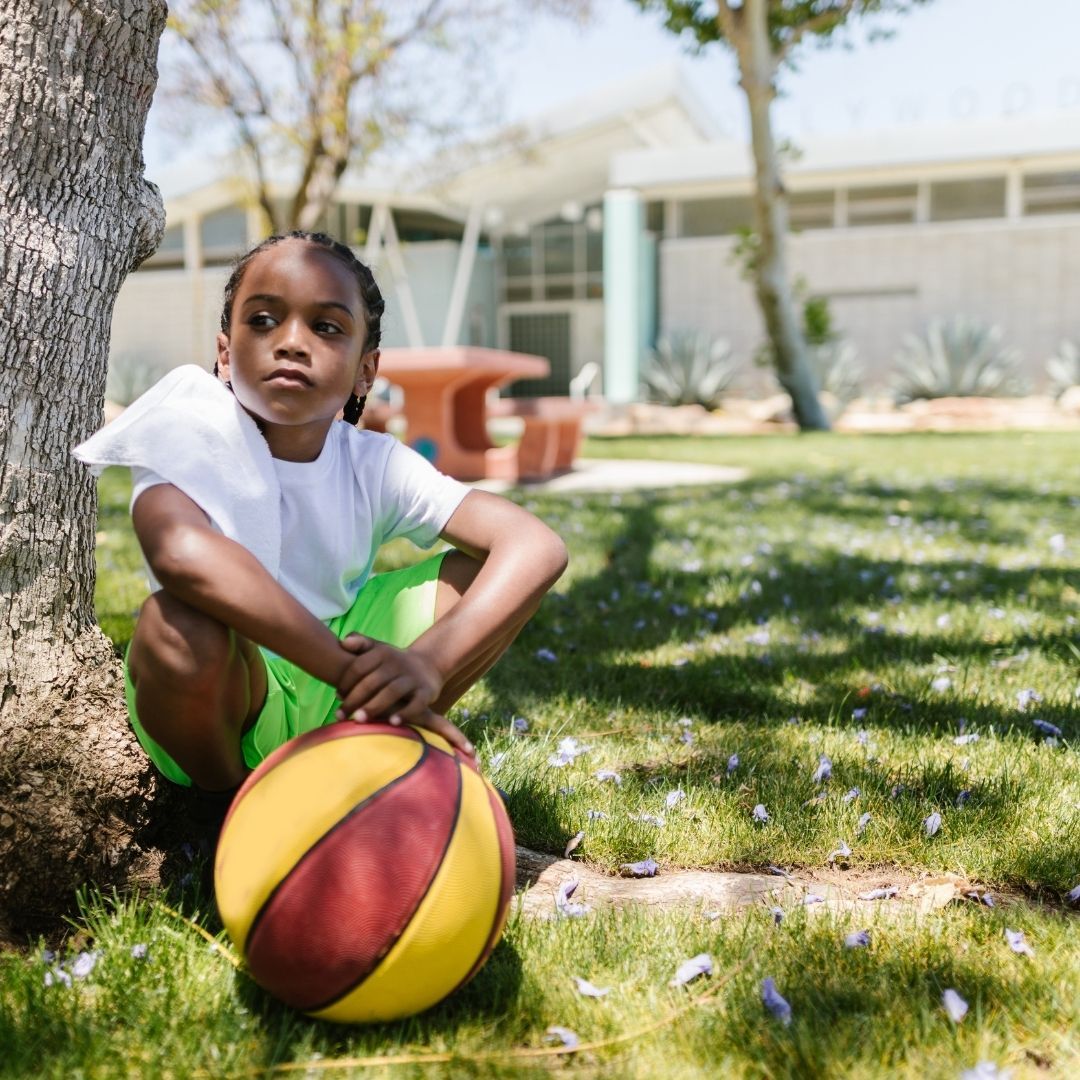 a child sitting next to a tree with a basketball