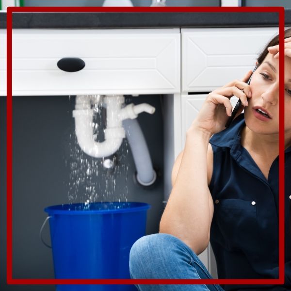 A distressed woman calls for an emergency plumber in San Diego as a pipe leaks water into a bucket under her kitchen sink. A distressed woman calls for an emergency plumber in San Diego as a pipe leaks water into a bucket under her kitchen sink.