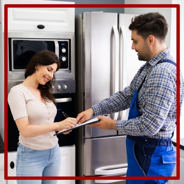 A satisfied female customer signing a clipboard presented by a Plumbing Plus plumber after a successful service call in her kitchen. A satisfied female customer signing a clipboard presented by a Plumbing Plus plumber after a successful service call in her kitchen.
