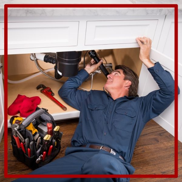 A thorough plumber lies on the floor to inspect the garbage disposal and pipes under a kitchen sink with a flashlight. A thorough plumber lies on the floor to inspect the garbage disposal and pipes under a kitchen sink with a flashlight.