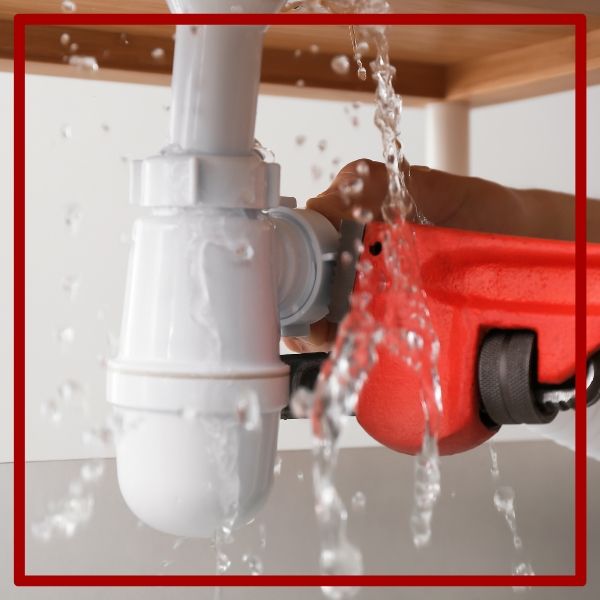 A close-up of a plumber making an emergency repair with a red wrench on a leaking white PVC pipe under a sink. A close-up of a plumber making an emergency repair with a red wrench on a leaking white PVC pipe under a sink.