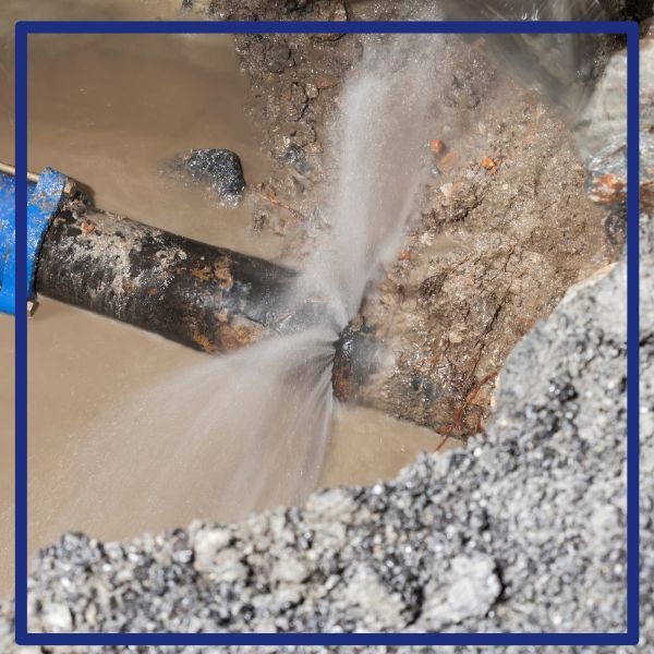 An emergency plumber addressing a major underground pipe burst, with water spraying from a rusty main line. An emergency plumber addressing a major underground pipe burst, with water spraying from a rusty main line.