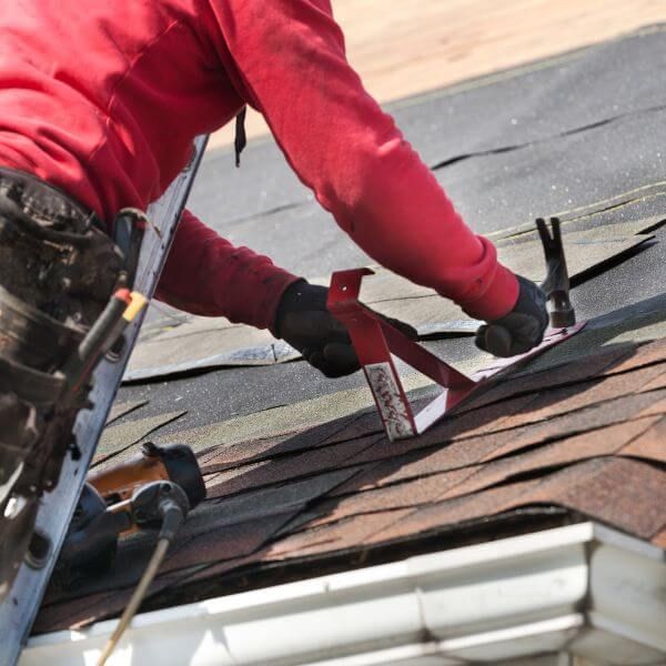 A roofer wearing a red hoodie installing shingles