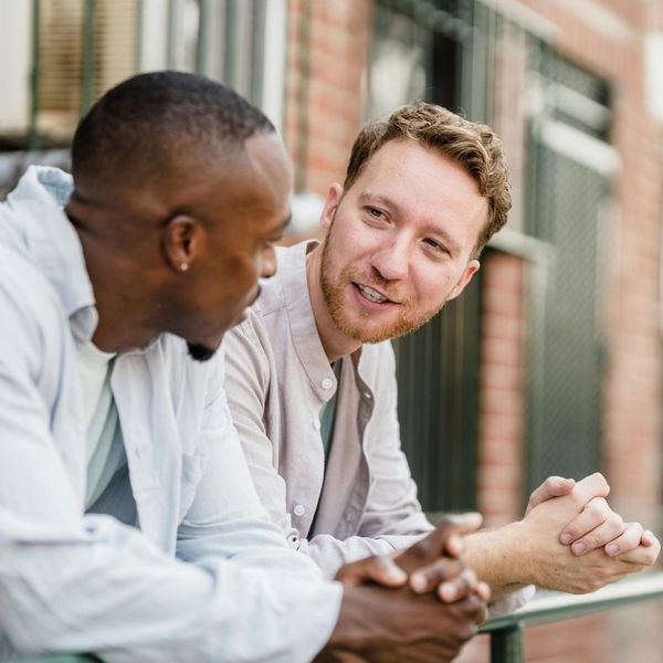 Two men, smiling and engaged in a supportive, casual conversation outdoors.