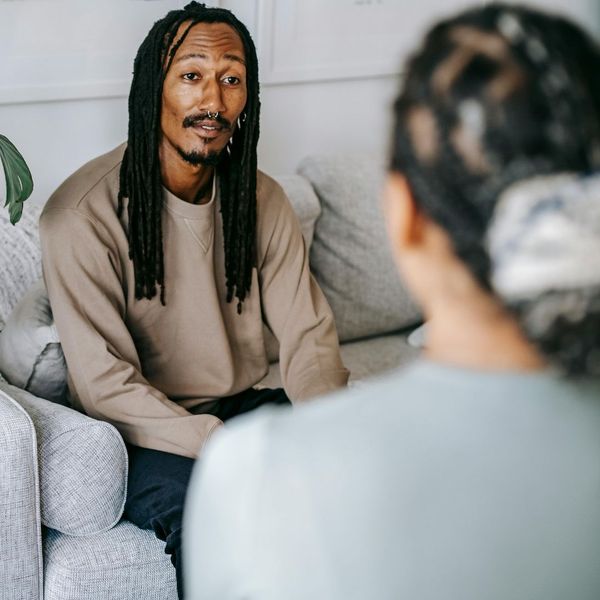 A man on a sofa, speaking earnestly to an unseen person during what appears to be a one-on-one therapy or deep conversation.