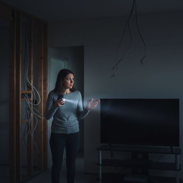 a homeowner looks worriedly at a darkened room in a newly built house, holding a flashlight