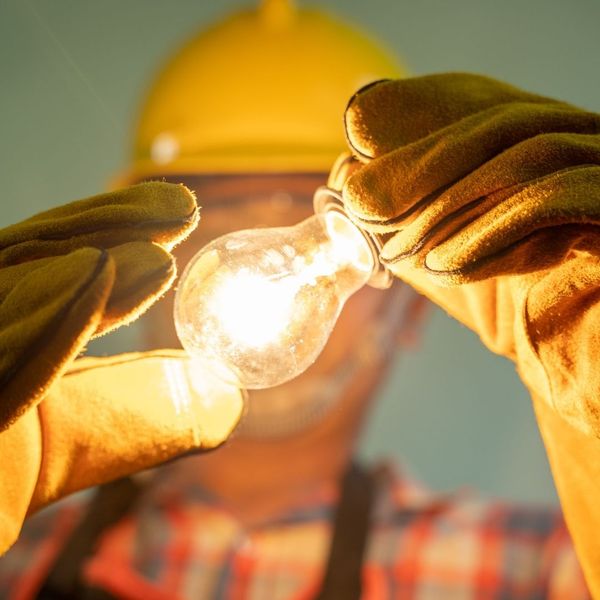 Expert hands working on electrical wiring holding an illuminated light bulb Expert hands working on electrical wiring holding an illuminated light bulb