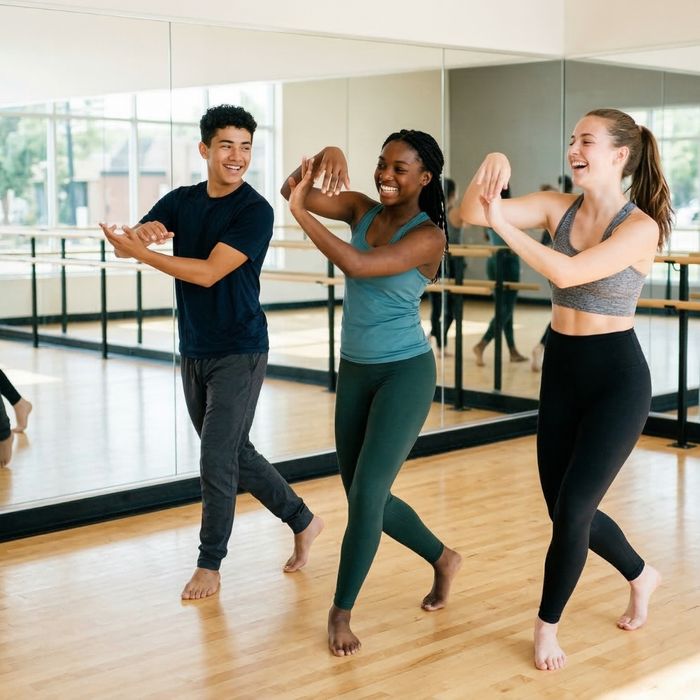 A young teenage girl laughs warmly while a dance instructor gently corrects her posture at the barre in a bright studio