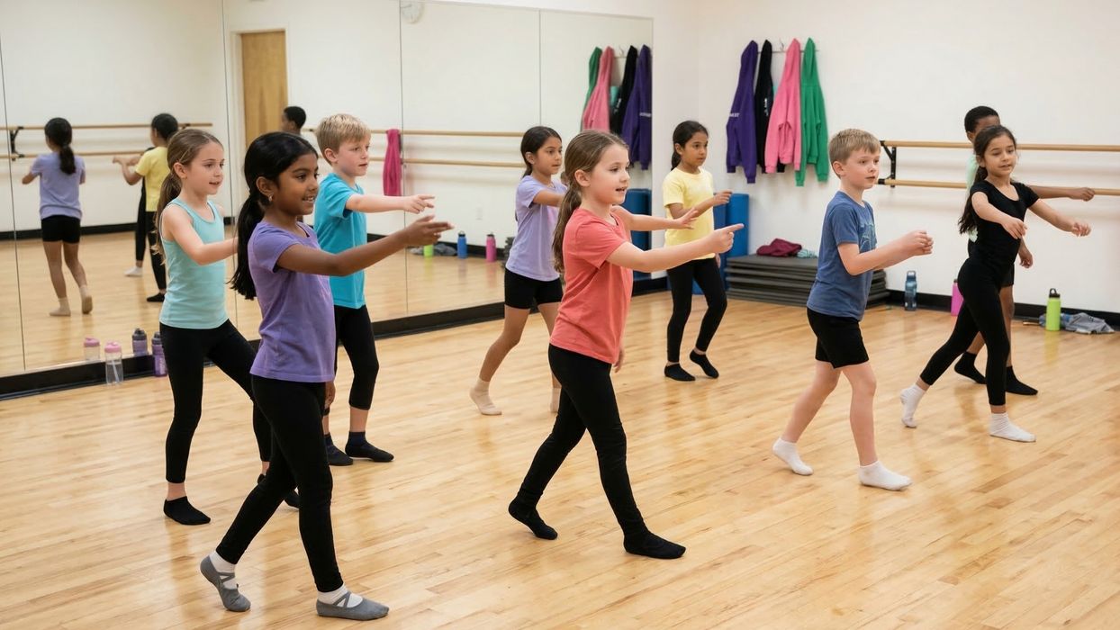 A group of smiling diverse children in a brightly lit dance studio practicing a group routine together.