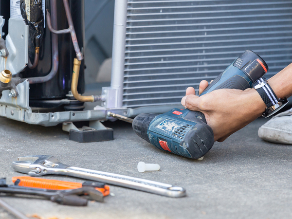  Technician using a drill to fix a modern AC system.