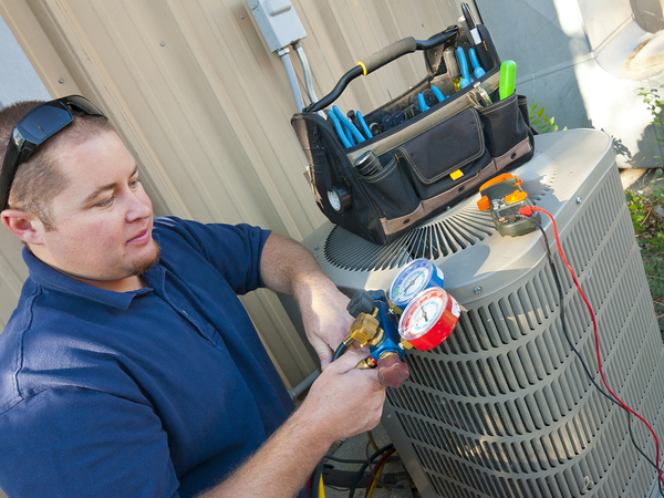 Air conditioner repair man checking levels on an air conditioning unit.