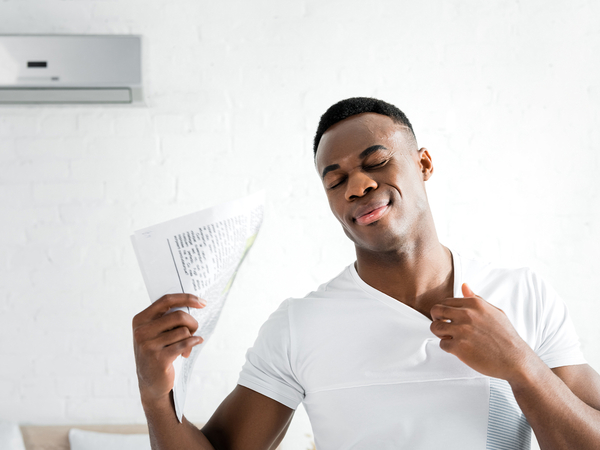 African American man hot inside of his home; fanning a newspaper in front of AC.