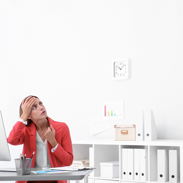 ​​Young woman suffering from heat under broken air conditioner in office.