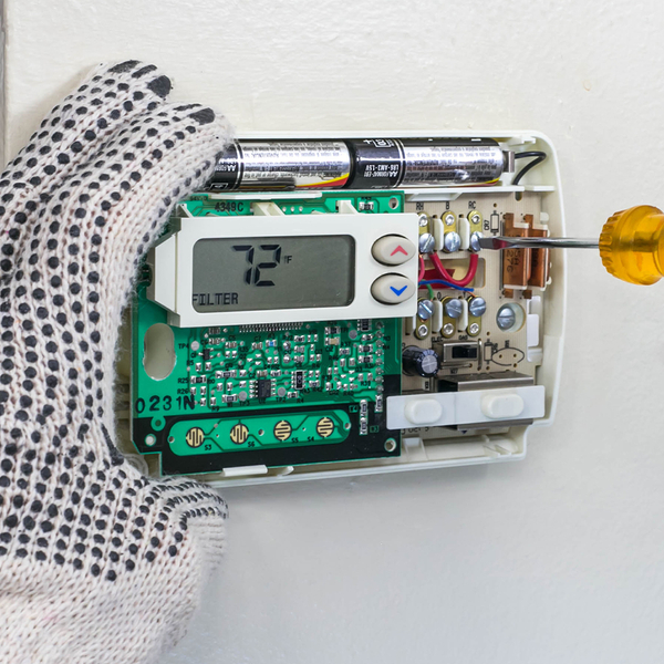 HVAC repairman’s gloved hands installing digital thermostat with screwdriver.