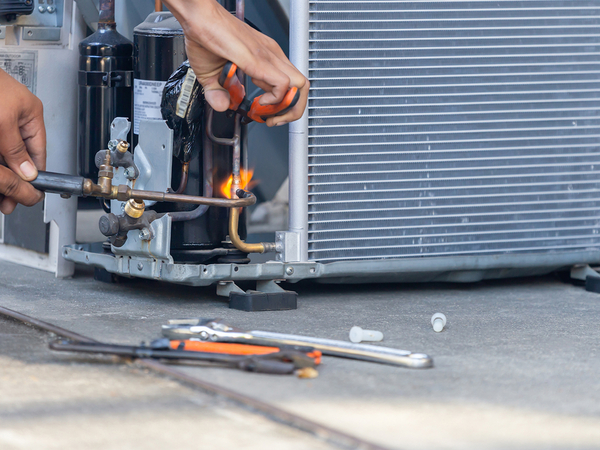 Air conditioning repair technician using a welder to fix a unit.