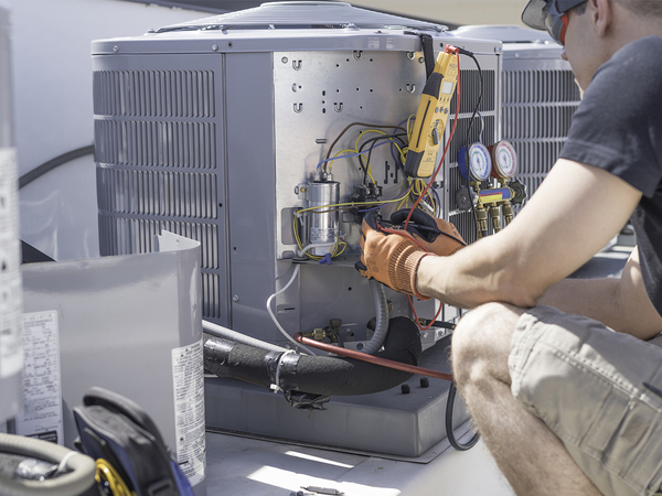 Hvac repair technician using a voltmeter to test components on an air conditioner condenser.