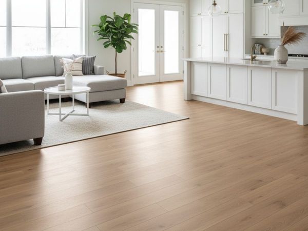 Open concept living room and kitchen with light wood-look flooring, comfortable grey sectional, and white kitchen cabinets, showcasing a bright and modern interior.