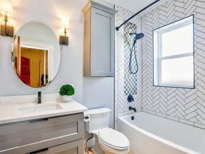 Newly renovated bathroom with herringbone pattern subway tile in the shower and white and grey geometric accent tile, featuring a modern tub and vanity.