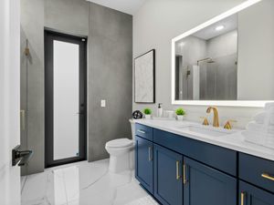 Stylish bathroom with a dark blue vanity, white countertop, gold-finish faucet and hardware, and a large illuminated mirror, showcasing modern fixtures and lighting.
