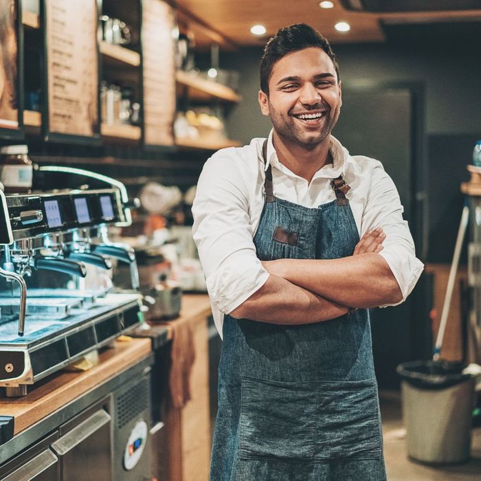A cafe owner laughing with his arms crossed behind the counter of his business
