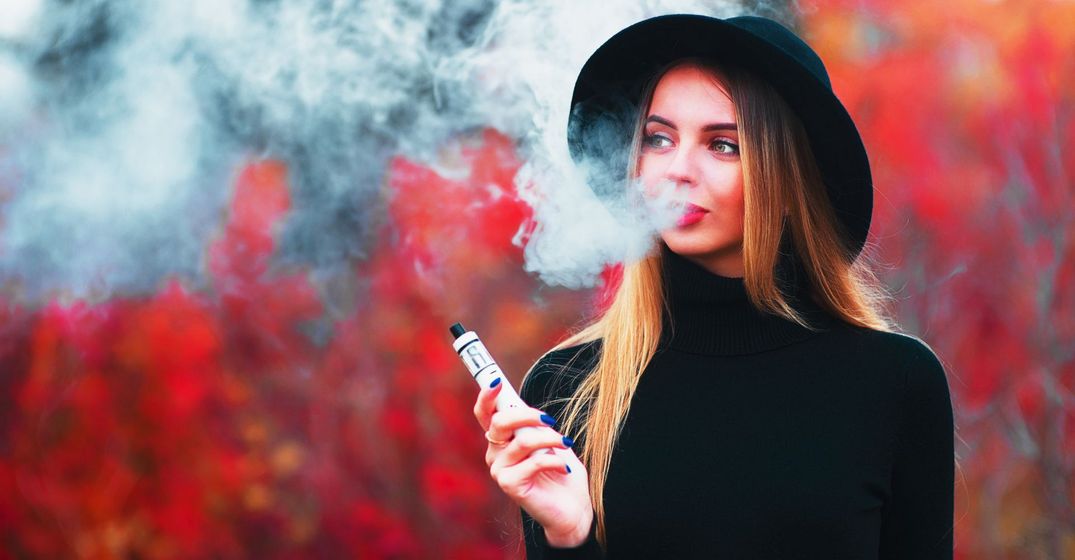 Lady in black clothing smoking a vape in a red forest