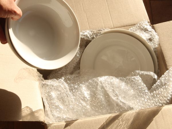 photo of person packing glass plates into moving boxes