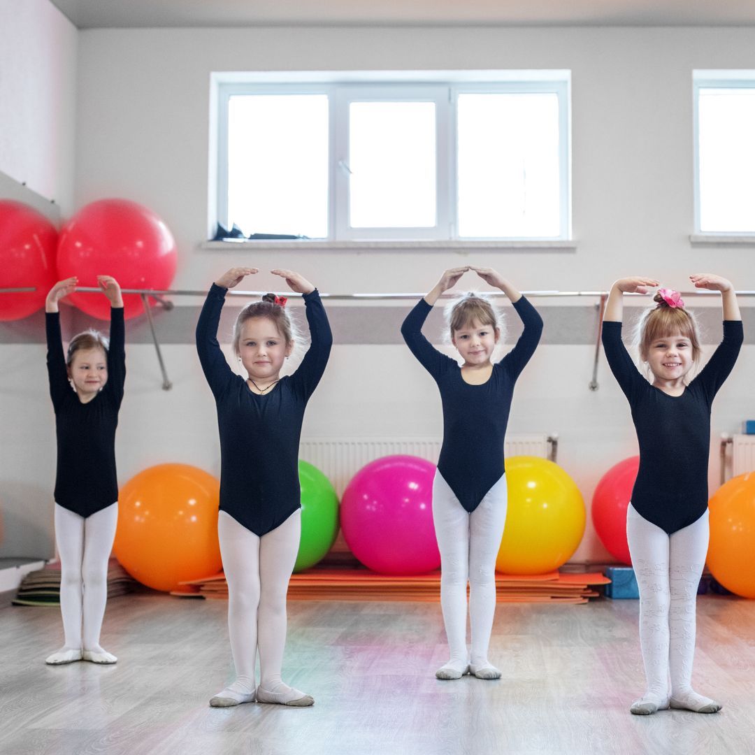 Four young girls smiling and posing in a ballet class. 