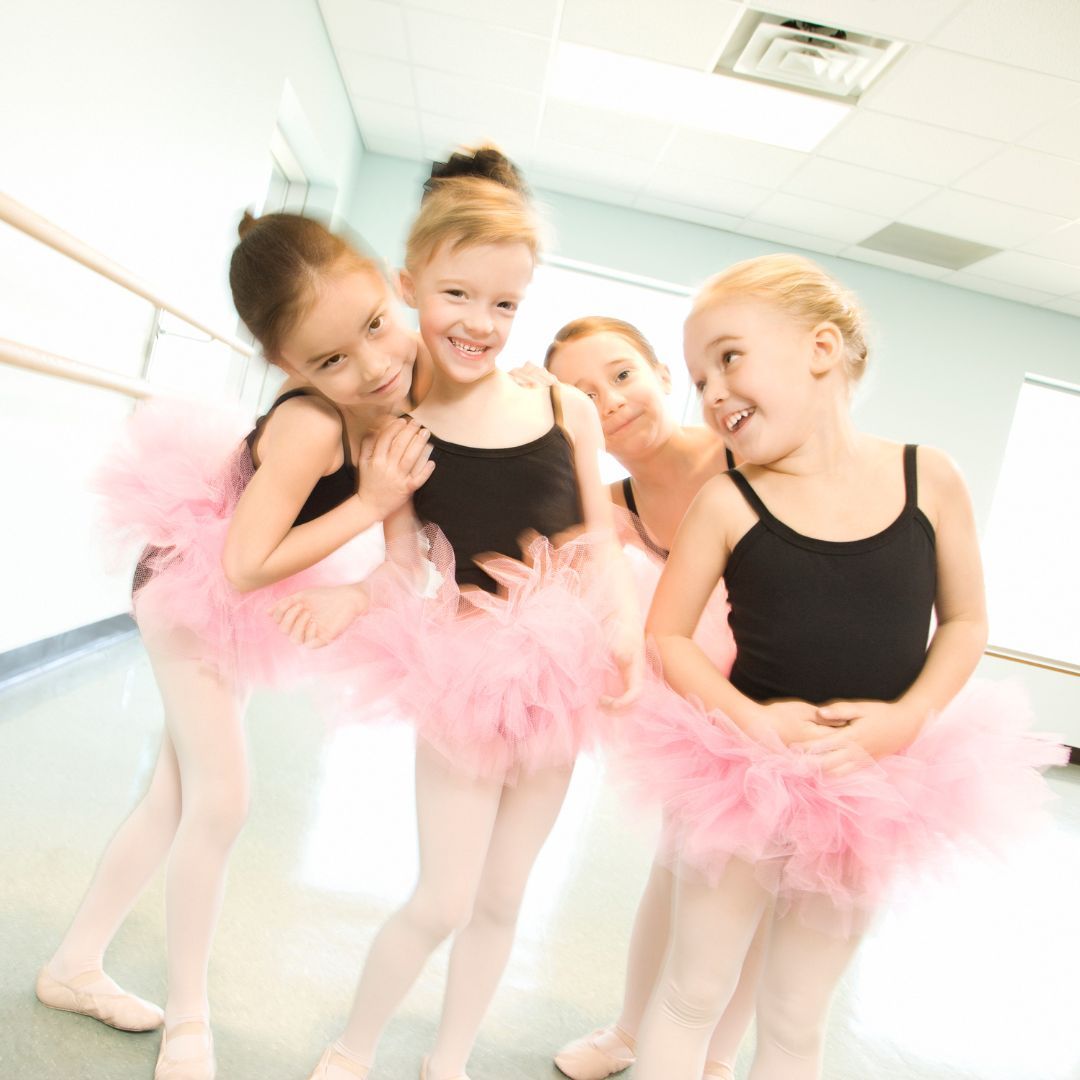 Four young girls wearing black leotards and pink tutus.