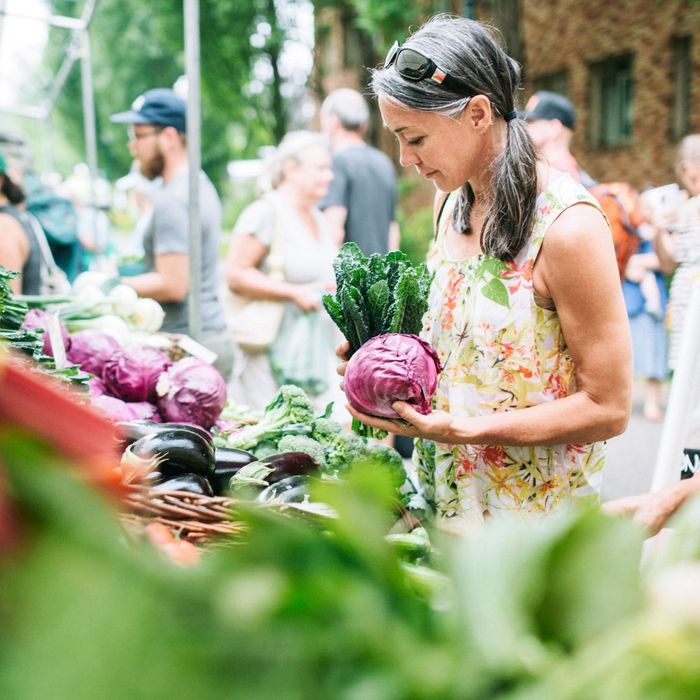 Person holding vegetables and standing near a produce booth at a farmers market