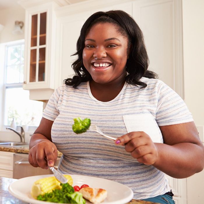 smiling woman eating chicken and vegetables