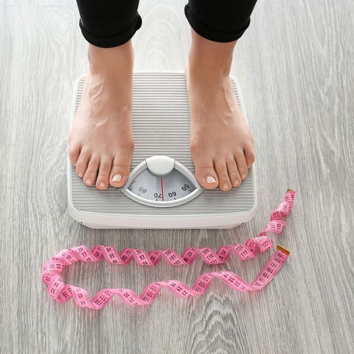 person standing on scale in front of measuring tape