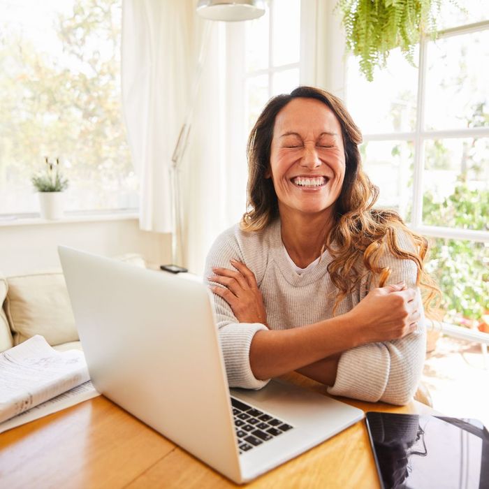 Person with a smile and eyes scrunched closed sitting at a table with a laptop