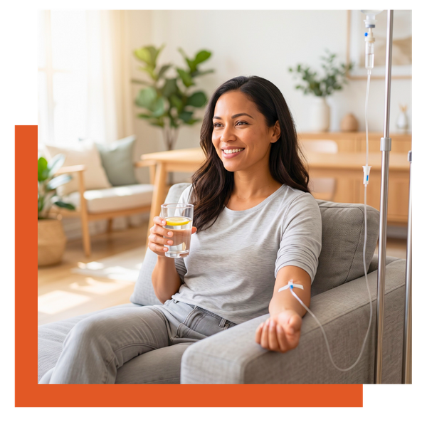 Smiling woman holding a glass of lemon water while receiving in-home IV hydration therapy.