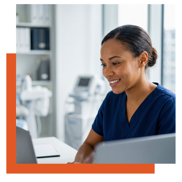 Smiling female healthcare professional looking at a laptop screen in a modern medical office.