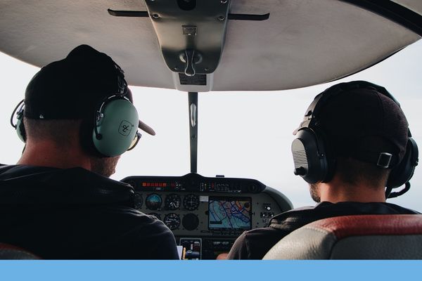 Two pilots or an instructor and student wearing headsets, looking forward in the cockpit during a flight.