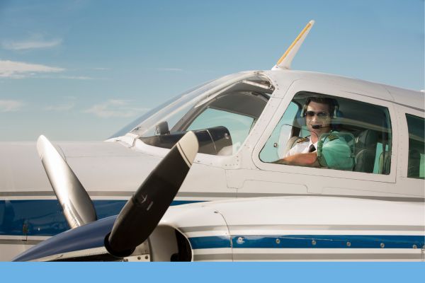 A smiling pilot in a headset sitting in the cockpit of an aircraft ready for flight.