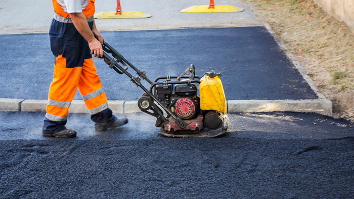 Worker Using a Vibratory Plate Compactor on Asphalt Road