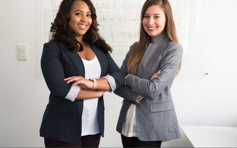 Two women with their arms crossed and smiling in business casual attire