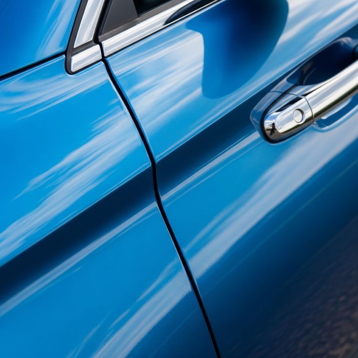 A close-up, angled shot of a metallic blue car door, reflecting the sky clearly to highlight its deep gloss and shine.