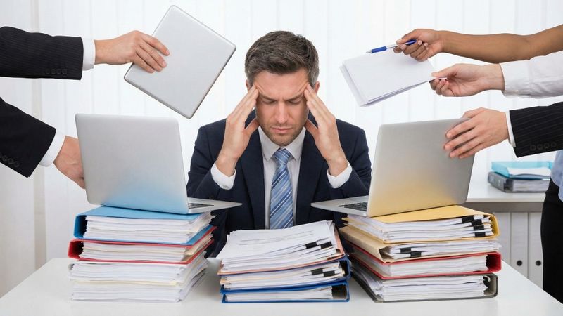 A stressed executive at a cluttered desk with many hands reaching in with more work. A stressed executive at a cluttered desk with many hands reaching in with more work.