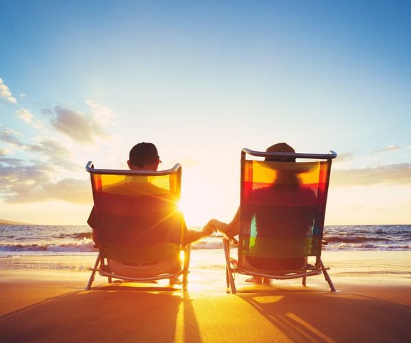 Serene image of a couple holding hands while sitting in lounge chairs on the beach as the sun sets