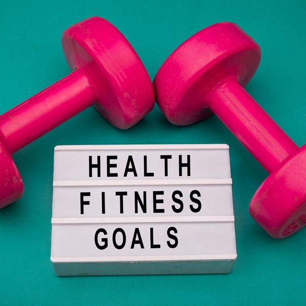 Two pink weights with a sign that says "Health Fitness Goals."