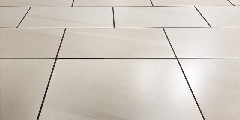 A low-angle shot of clean, light-colored tile flooring with perfectly straight, dark grout lines, showcasing the pristine finish of color sealing.