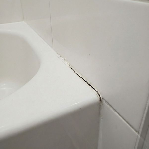 visible crack runs along the grout line in the corner where a white tub meets the tiled wall