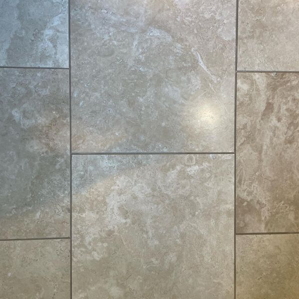 A close-up shot of light beige, textured porcelain tiles arranged in a varied rectangular pattern with clean, perfectly applied grout.